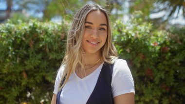 Güneşli bir günde şehir parkında gülümseyen çekici sarışın kadın..