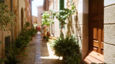 Mallorca 'nın güneşli bir arka sokağının görüntüsü bulanık. Yürüme yolu bitkilerle kaplı. İnsanlar uzaklardan tipik bir Akdeniz sokağının özünü yakalıyor..