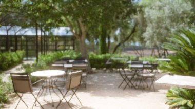 Mallorca 'da açık hava kahve seti. Parlak güneş ışığı altında odağını kaybetmiş masalar, sandalyeler ve yemyeşil alanlar..