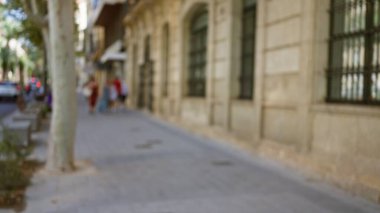 Güneşli bir günde tarihi binanın yakınında yürüyen insanların bulunduğu bulanık şehir sokak sahnesi, bokeh etkisi ve odaklanmış arka plan.