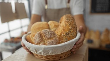 Kapalı bir fırın ortamında içi ekmek dolu sepet tutan adam, rahat bir dükkanın iç dekorunda yeni, zanaatkar ürün gösterisini vurguluyor..