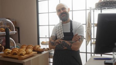 Pastanenin içinde kolları çapraz duran dövmeli ve sakallı yakışıklı İspanyol bir adam.