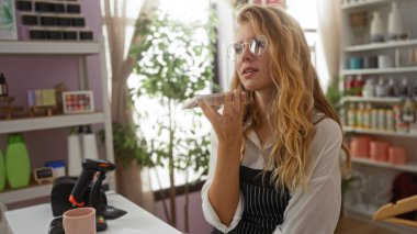 Dekor dükkanında arka planda dekorasyon malzemeleriyle dolu raflarla konuşan genç bir kadın.