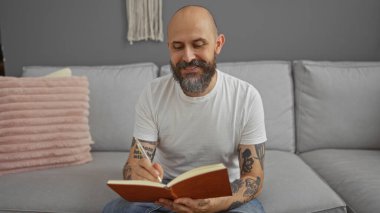 Günlüğüne sakallı kel adam rahat evinin modern oturma odasında gri koltukta otururken