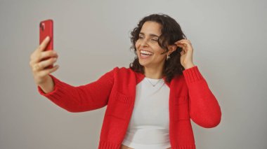 Genç İspanyol kadın gülümserken ve saçlarını tutarken selfie çekiyor, beyaz bir arka planda izole edilmiş..