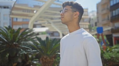 Güneşli bir günde şehir parkında arka planda modern şehir binaları olan yakışıklı İspanyol bir adam..