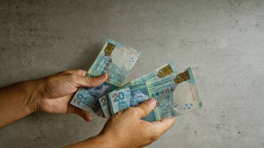El ele tutuşan Hong Kong doları banknotları somut bir arka plana karşı, finans ve döviz kurunu vurguluyor