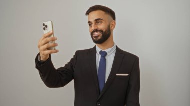 Takım elbiseli yakışıklı İspanyol bir adam akıllı telefonuyla özçekim yapıyor ve beyaz izole edilmiş bir arka plana karşı.