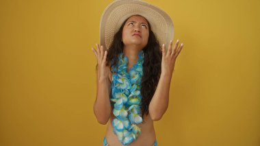 Ley takan ve güneş şapkalı bir kadın, izole edilmiş sarı arka planda hayal kırıklığına uğramış bir ifadeyle yukarı bakıyor.