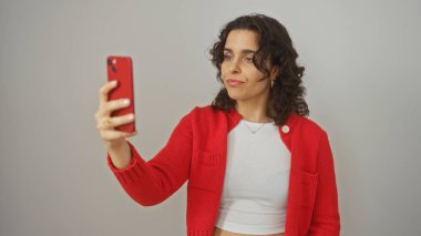 Kırmızı kazaklı, esmer, genç ve çekici bir kadın izole edilmiş beyaz arka plan üzerinden telefonuyla selfie çekiyor..