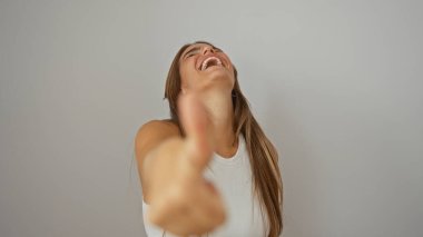 Genç bir kadın neşeyle gülüyor ve olumlu bir jest yapıyor, beyaz bir arka plan duvarından izole edilmiş, pozitif ve kendinden emin titreşimler yayıyor.