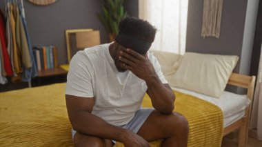 Yatak odasında yatağında sakallı, yüzünü kapalı bir evde örten Afro-Amerikalı genç bir adam..