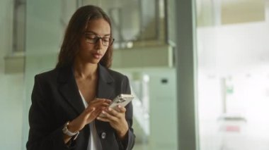 Modern ofis ortamında akıllı telefon kullanan bir kadın iş elbisesi ve gözlük takarken hayal kırıklığını dile getiriyor.