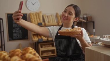Bir kadın pastanede elinde ekmek dolu bir sepet hamur işi tutarken selfie çekiyor.