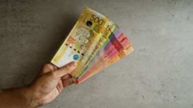 Beton bir arka plan üzerinde renkli Filipinli peso banknotları yelpazesini tutan bir el..