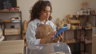 İspanyol kadın fırında çalışıyor taze ekmek ve hamur işleri arasında tablet kullanıyor.