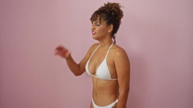 Bikini giyen genç bir kadın iletişim kurmak için el ve ağızla yüksek sesle bağırıyor, izole edilmiş pembe arka planda çığlık atıyor. İfadesinde İspanyol güzeli.