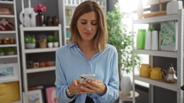 Kapalı yumrukla kutlama yapan bir kadın, ev dekorasyonu mağazasında akıllı telefon ve raflarda çeşitli dekorasyon ürünleri kullanarak kutluyor.