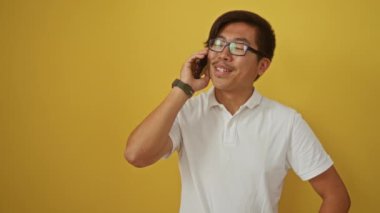 Gözlüklü genç adam sarı arka planda telefonla konuşuyor.