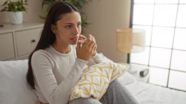 Sıcak bir yatak odasında, elleri yüzü kapalı bir şekilde bir yatakta oturan İspanyol kadın, sade bir atmosfer içinde bir üzüntü ya da üzüntü anı olduğunu ima ediyor..