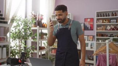Dekoratördeki genç adam telefonuna gülümsüyor ve şık dekorasyonlar ve çeşitli ürünlerle çevrili heyecanla alkışlıyor..