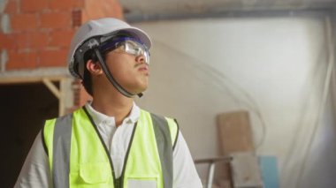 Çin 'de bir inşaat sahasında çalışan güvenlik yeleği ve sert şapkalı genç adam, ev içinde bir yapı inşa etmek için gayret ve kararlılık gösteriyor..