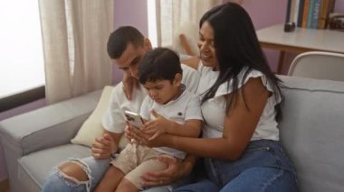 Latin bir aile, bir erkek, bir kadın ve bir çocukla birlikte rahat bir oturma odasında bir kanepede oturuyor, akıllı bir telefonla iletişim kuruyor..