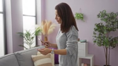 Akıllı telefon ve kredi kartını modern dekorlu rahat bir oturma odasında tutan kadın rahat ve şık bir atmosfer sunuyor. Evde gezinmek ve alışveriş yapmak için mükemmel..