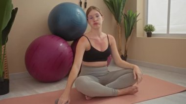Spor salonunda halterle egzersiz yapan bir kadın. Huzurlu bir iç mekanda yoga minderinin yanında oturmuş spor yapıyor.