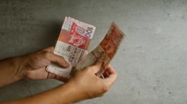 Hong Kong doları sayan bir adam iki eliyle beton bir arkaplan tutuyor.