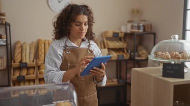 Fırında tablet kullanan kadın raflarda çeşitli ekmekler ve sergilenen glütensiz hamur işleri ile