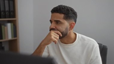 Ofiste çalışan genç bir adam. Masada otururken düşünceli ve düşünceli görünüyor.