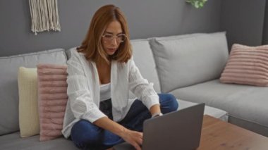 Oturma odasında dizüstü bilgisayarla çalışan esmer bir kadın. Gözlüklerini çıkarırken yorgun görünüyor..