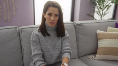 Kadınlar, rahat oturma odasındaki kanepede oturan, gri bir kazak giyen, modern dekor ve yumuşak yastıklarla çevrili, ciddi bir yüz ifadesi sergileyen hayır hareketleriyle hareket ederler..