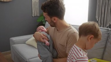 Baba kucağında bebekle evin içinde oynayan bir çocuk evde hassas bir aile anını yakalıyor.