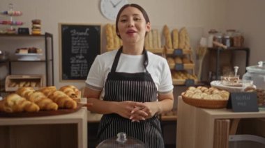 Fırındaki genç esmer kadın hamur işleri, ekmek ve sıcak gülümsemeli glütensiz ürünler sunuyor..