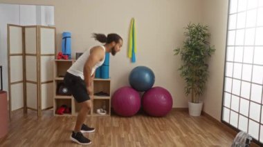 Sağlıklı yaşam salonunda egzersiz yapan bir adam spor aletleriyle çevrili burpee 'ler yapıyor. Sakin bir iç mekanda güç ve denge sergiliyor..