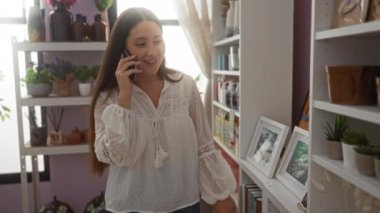 Ev dekorasyonu mağazasında dekorasyon malzemelerine bakarken telefonla konuşan genç bir kadın.