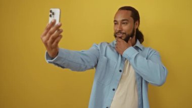 Akıllı telefonlu selfie çeken bir adam canlı sarı arka planda modern yaşam tarzını ve bağlantısını yakalıyor..