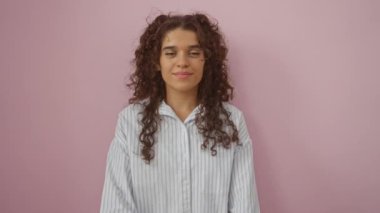 Kıvırcık saçlı İspanyol kadın çizgili gömlekli pembe bir duvara dayanıyor.