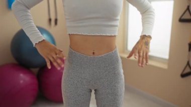 Spor kıyafetleri içinde spor salonunda duran genç bir kadın ellerini beline koydu.