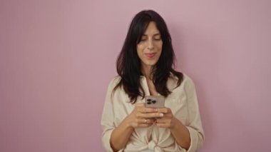 Koyu renk saçlı güzel bir kadın akıllı telefon tutuyor ve pembe bir arka plan önünde gülümserken iyi bir jest yapıyor.