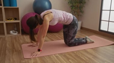 Beden dersinde yoga yapan kadın, kapalı alanda aktif yaşam tarzı egzersizi yapan kararlı esmer kadına odaklanmış.