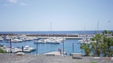 Bulanık yatları ve açık mavi gökyüzünün altında arka planda insanları olan bir marinanın odaksız görüntüsü