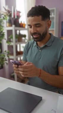 Çiçekler ve dekorasyonlarla çevrili ev dekorasyonu mağazasında gülümseyen ve telefonu kullanan genç bir adam..