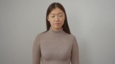 Uzun saçlı bir kadın beyaz bir arkaplanda balıkçı yaka kazak giyip düşünceli bir ifadeyle yukarıya bakıyor ve izole edilmiş bir şekilde duruyor..