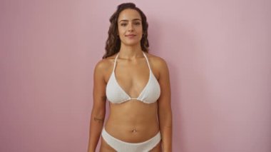 Gülümseyen, bikinili genç bir kadın. Gözleri kapalı, gözleri kör bir vaziyette, izole edilmiş pembe arka planda.