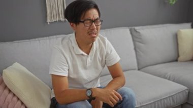 Evdeki gri bir kanepede otururken beyaz gömlekli genç adam kötü kokudan burnunu kapatıyor.