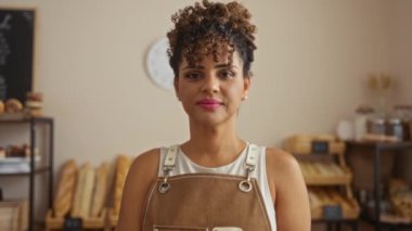 Fırında kameraya gülümseyen bir kadın. Arkasında ekmek rafları var.