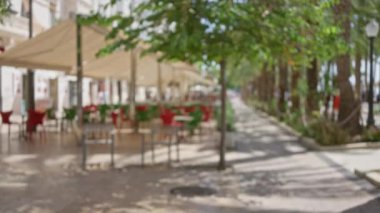 Yeşil ağaçların ve güneşli bir atmosferin ortasındaki bulanık Bokeh kentsel ortamında gündüz vakti dışarıda kırmızı sandalyeleri olan odaksız bir kafe..